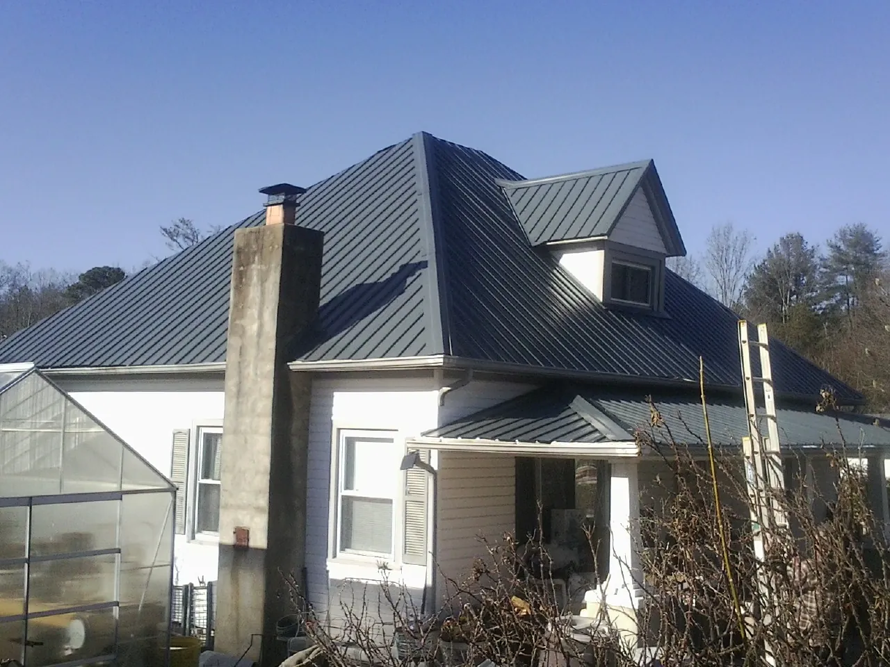 Dark blue standing seam metal roof on a white farmhouse with dormer — Slate & Tile Roof Repair by Roofing Brothers in Pine Mountain Valley