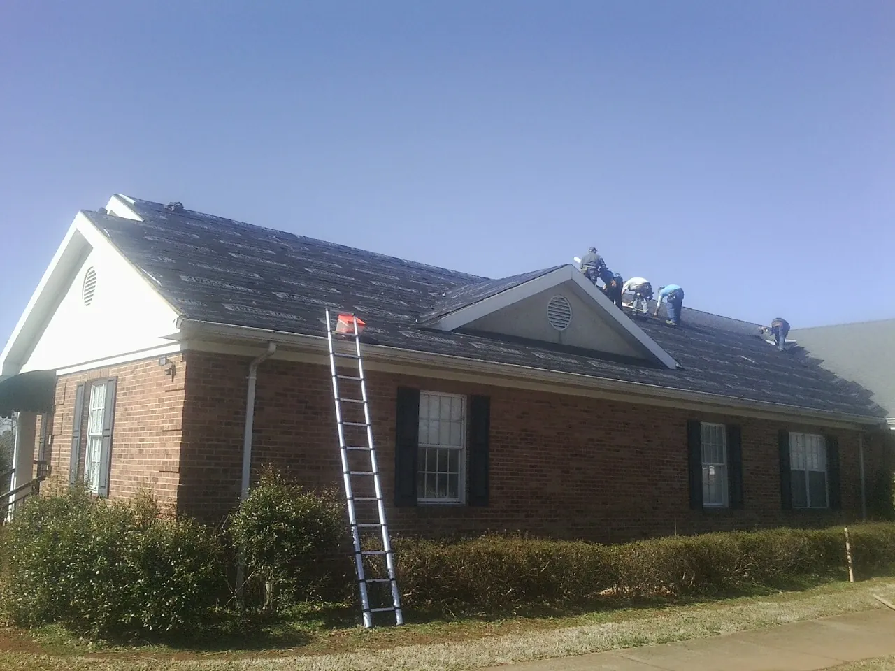 Crew tearing shingles off a brick ranch roof with a ladder set — Emergency Roof Repair work by our crew in Pine Mountain Valley