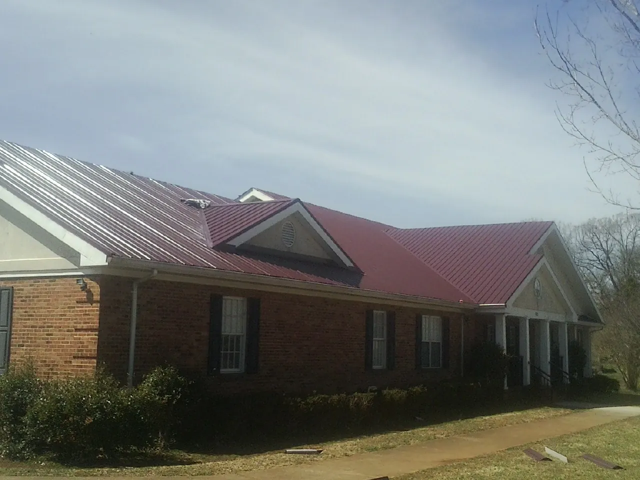 Red metal roof with gabled entries on a long brick building, from a Hail Damage Roof Repair job in Pine Mountain Valley