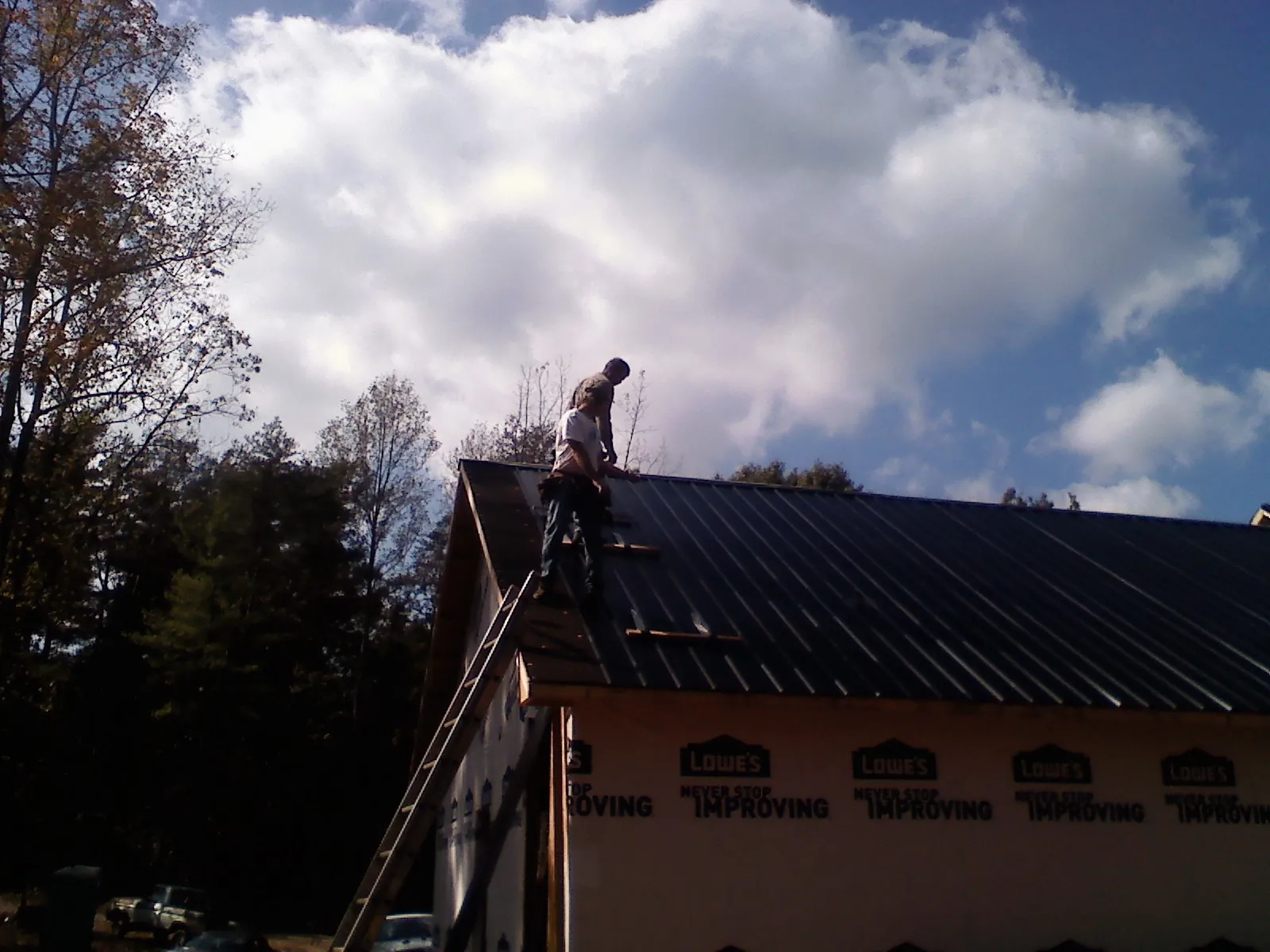 Roofer fastening dark metal panels high against a cloudy sky, from a Roof Inspection job in Pine Mountain Valley