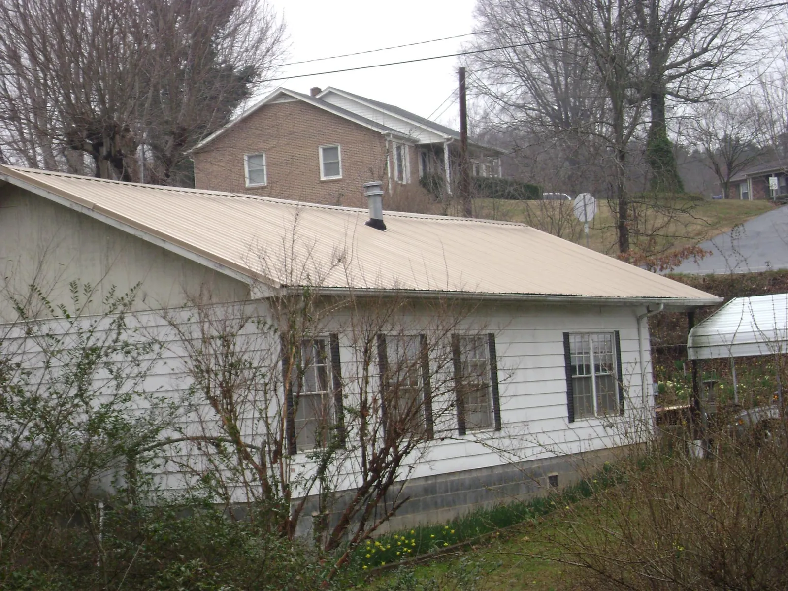 Tan metal roof on a white sided house set into a hillside — Commercial Roofing by Roofing Brothers in Pine Mountain Valley
